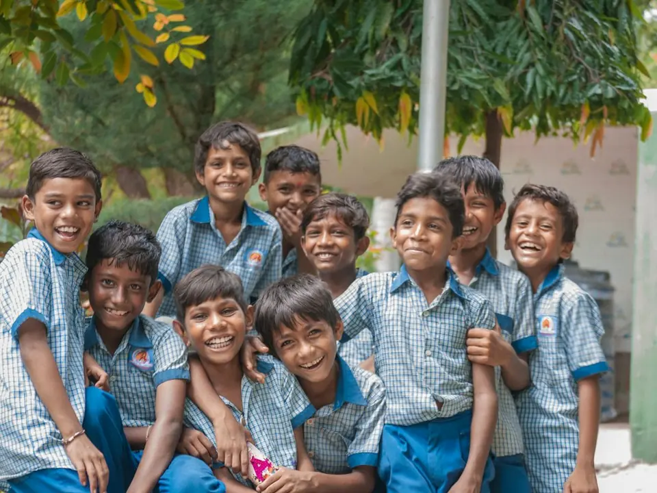 A group of smiling schoolboys in blue checked uniforms sitting close together outdoors (stock photo).