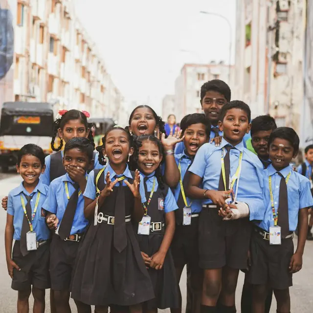 A group of smiling students in blue uniforms and ID lanyards, posing together on a street (stock photo).