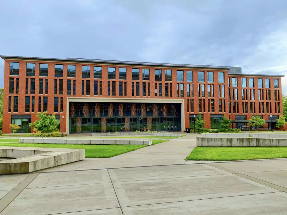 A modern red-brick school building with lawns and a paved walkway under a blue sky (stock photo).