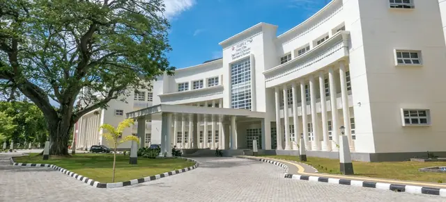 A large white school building with columns and a curved drive, with a big tree on the left (stock photo).