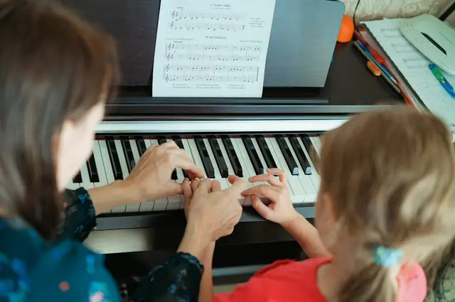 A teacher’s hands guiding a child’s hands on a piano keyboard, with sheet music above (stock photo).