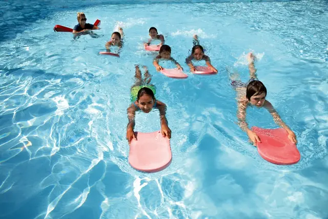 Children swimming across a sunny pool holding pink kickboards (stock photo).